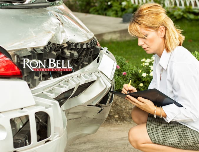 An insurance adjuster looking at the damaged bumper of a car