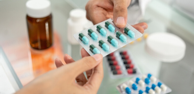 Bad-Drugs hand passing sleeve of blue an green pills to another hand